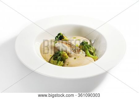 Sea cod fillet close up. Served cuisine. Dish with fish and baked broccoli puree ingredients in white plate isolated. Luxury culinary. Restaurant food portion, delicious supper, main course