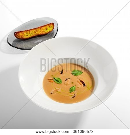 Chilean mussels soup in white bowl. Served main course close up. Seafood cream soup with roasted bread slice. Restaurant food portion, main course with toast. Dinner, gourmet meal in plate