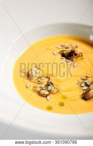 Pumpkin soup in white bowl. Served main course close up. Vegetable cream soup decorated with seeds. Restaurant food portion, main course. Vegetarian supper. Dinner, gourmet meal in plate