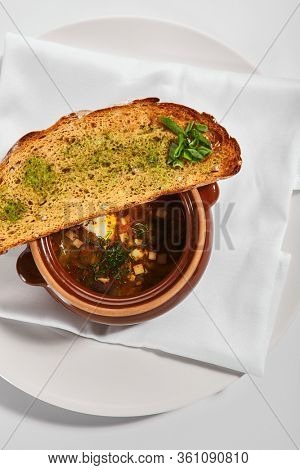 Oven baked meat soup with artichokes in pot. Delicious hot pottage with fresh bread and greenery. Traditional cuisine, restaurant dish, dinner food. Aromatic goulash on white napkin