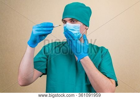 Surprised Doctor In Green Suit And Blue Mask And Gloves With Thermometer In Hand On Yellow Backgroun