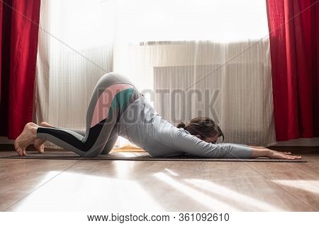 Woman Exercising Yoga In A Room Maling A Puppy Pose Or Uttana Shishosana.