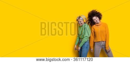 Curly Haired Friends Listening To Music Using Headphones On A Yellow Freespace While Dancing Happily