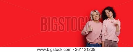 Caucasian Girls Dressed In The Same Clothes Are Posing On A Red Wall With Freespace Gesturing The Li