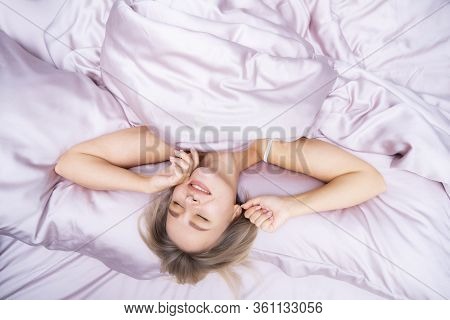 Beautiful Blonde Wakes Up In Bed. Rest At The Hotel. A Young Woman Is Lying On Pink Satin Bedding. F