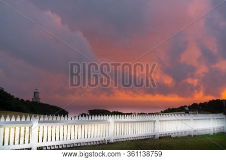 Dramatic Night Sky Red And Grey Clouds With Lighthouse In Distance Beyond White Picket Fence At The 