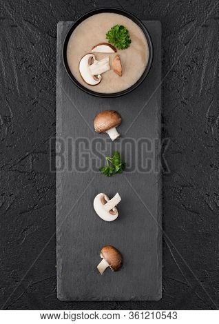 Black Bowl Plate Of Creamy Chestnut Champignon Mushroom Soup On Black Background With Black Stone Bo