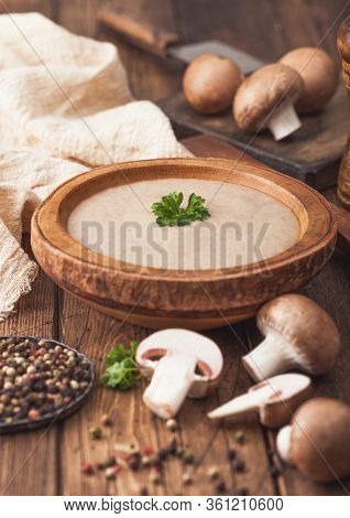 Wooden Plate Of Creamy Chestnut Champignon Mushroom Soup With Wooden Spoon, Pepper And Kitchen Cloth