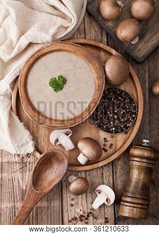 Wooden Plate Of Creamy Chestnut Champignon Mushroom Soup With Wooden Spoon, Pepper And Kitchen Cloth