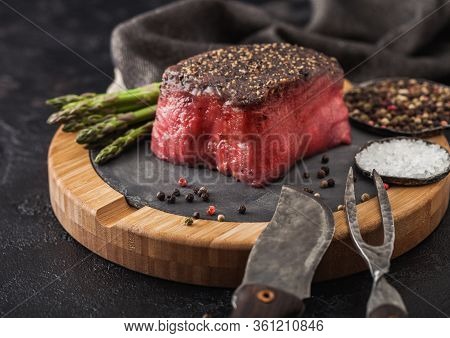 Slice Of Raw Beef Topside Joint With Salt And Pepper On Stone Chopping Board With Fork And Knife, As