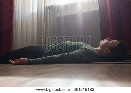 Older Woman Rests On The Floor Of The Living Room In Savasana Or Corpse Pose