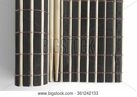 Chinese Sticks Lie On A Black And White Partially Twisted Bamboo Wooden Rug. Objects For Sushi. View