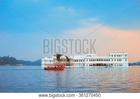 Romantic luxury India travel tourism - tourist boat in front of Lake Palace (Jag Niwas) complex on Lake Pichola on sunset with dramatic sky, Udaipur, Rajasthan, India