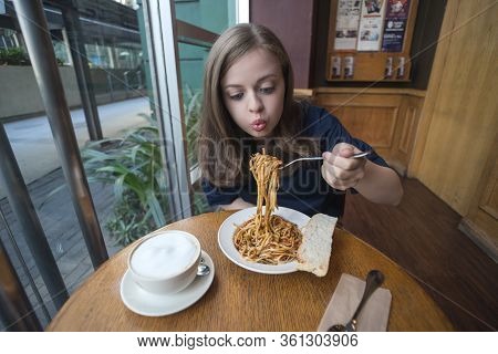 Young Caucasian Woman Girl Eating Italian Pasta With Funny Face Expression In A Cafe, Restaurant