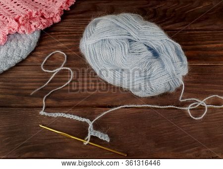 Crochet And A Skein Of Light Blue Wool Yarn, Top View On A Dark Wooden Background, In The Background
