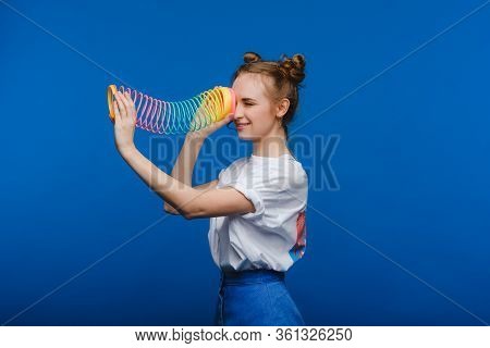 Beautiful Young Girl Playing With A Rainbow Slinky, A Toy Of Her Childhood On A Blue Background