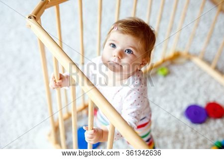 Beautiful Little Baby Girl Standing Inside Playpen. Cute Adorable Child Playing With Colorful Toys. 