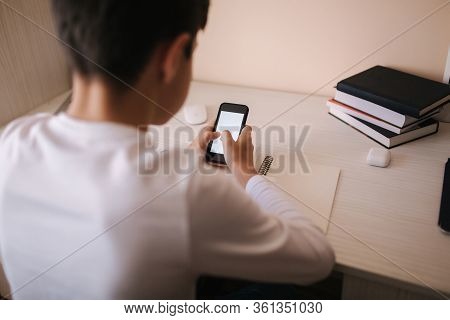 Schoolboy Study At Desk In His Room. Boy Use Laptop And Smartphone To Writing In Notebook. Books And