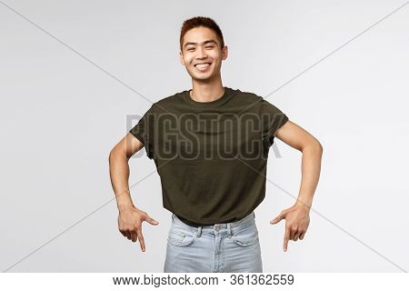 Portrait Of Cheerful Asian Man In Greey T-shirt, Laughing And Smiling Joyfully, Pointing Fingers Dow