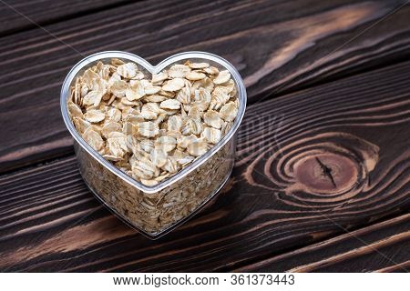 One Heart Of Oat-flakes, Uncooked Oats On Brown Wooden Board Background. Laconic Design. Symbol Of L