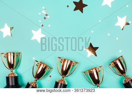 Golden Cups Of Winner With Shiny Confetti On A Blue Background With Copy Space. Flat Lay Style.