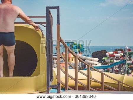 Closed Yellow Water Slide On The Background Of The Water Park. The Man Before The Descent. A Man Pre