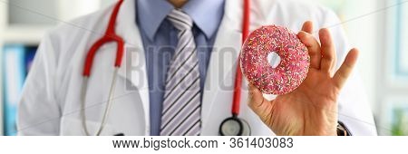 Doctor In Office Holding In Hand Pink Doughnut Close-up. Products That Can Not Be Consumed In Certai