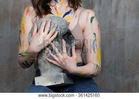 A Young Woman Who Has Gotten Dirty With Paint Holds A Sculpture Of A Man S Head With A Greek Profile