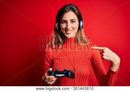 Young beautiful brunette gamer woman playing video game using joystic and headphones with surprise face pointing finger to himself