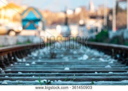 Closeup Of Old Overgrown Train Tracks Full Of White Pebbles. Blurred Outlines Of Train Vagons And Su