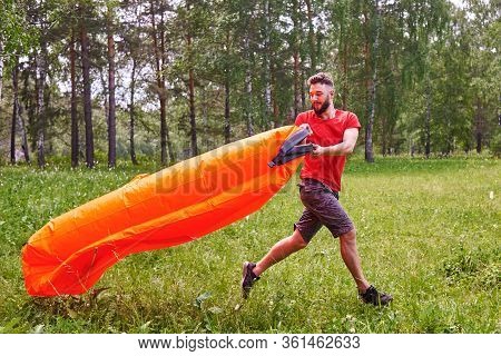 A Young Man Inflates A Lamzac With Air. A Man Inflates An Air Sofa. On The Background Of The Forest