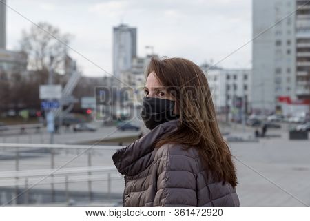 Woman Of European Appearance In A Black Medical Mask On Her Face From The Coronavirus Looks At The B