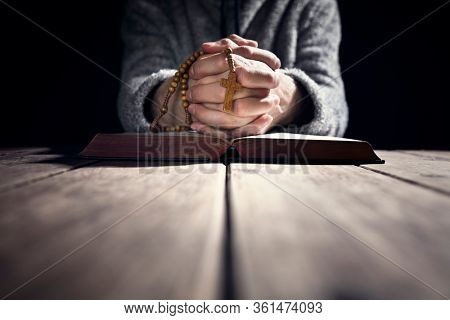 Hands folded in prayer on a Holy Bible in church concept for faith, spirtuality and religion