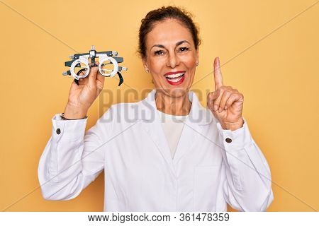 Middle age senior oculist woman holding optometrical glasses for vision correction surprised with an idea or question pointing finger with happy face, number one