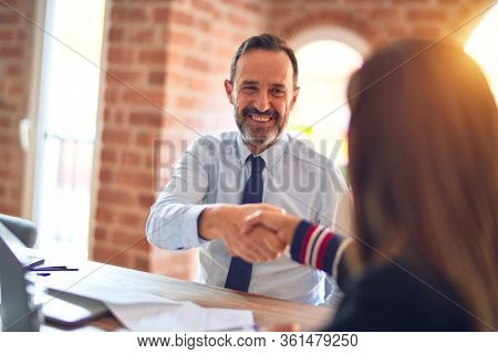 Two middle age business workers smiling happy and confident. Working together with smile on face using laptop doing handsake at the office