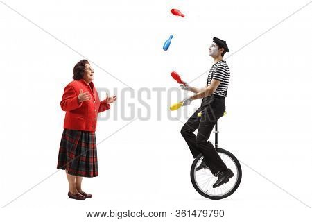 Full length profile shot of a senior woman watching a mime riding a mono-cycle and juggling isolated on white background