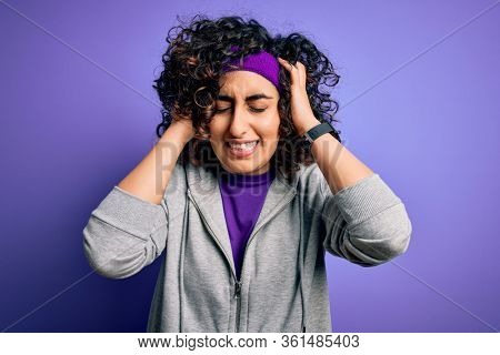 Beautiful curly arab sportswoman doing sport wearing sportswear over purple background suffering from headache desperate and stressed because pain and migraine. Hands on head.