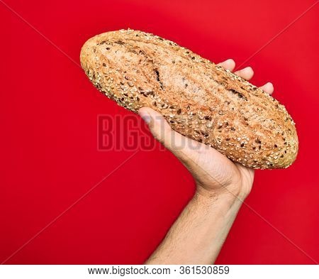 Beautiful hand of man holding wholemeal integral bread with cereals over isolated red background