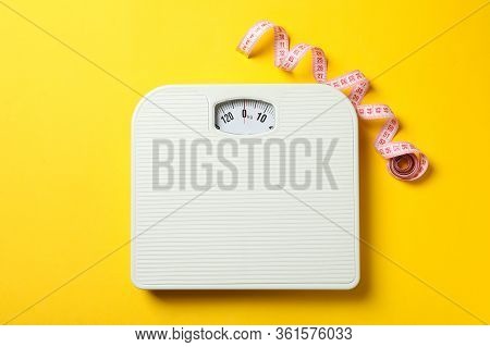 Scales And Measuring Tape On Yellow Background. Weight Loss Concept