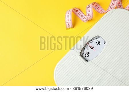 Scales And Measuring Tape On Yellow Background. Weight Loss Concept