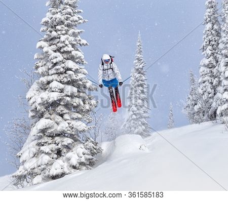 a Freerider in bright gear jumps between Christmas trees with a backflip element. prof skier in a be