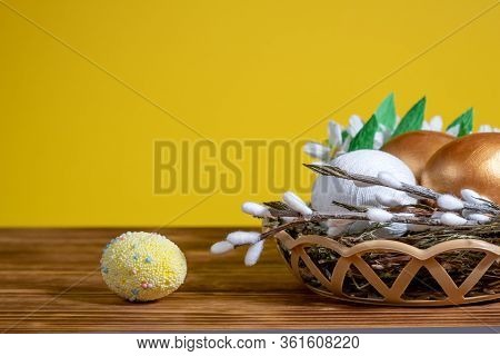 Easter Eggs In Basket Filled With Straw And Yellow Flowers And Willow. Preparation For Holiday. East
