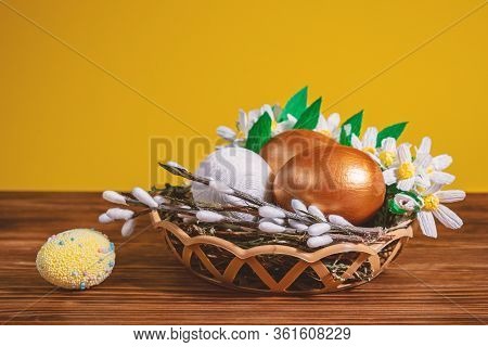 Easter Eggs In Basket Filled With Straw And Yellow Flowers And Willow. Preparation For Holiday. East