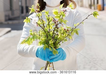 Girl Wearing Mask, Is Looking With Hope And Holding A Branch Of Blooming Twigs, Standing In The Midd