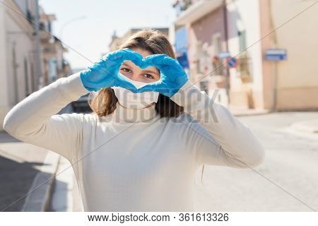 Girl Wearing Medical Mask, And Protective Gloves Gesturing Heart Shape Sign By Hands, Is Looking Wit