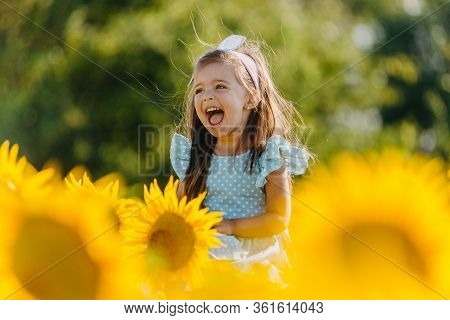 Little Cheerful Girl In A Field Of Yellow Sunflowers. Child And Sunflower, Summer, Nature And Fun. S
