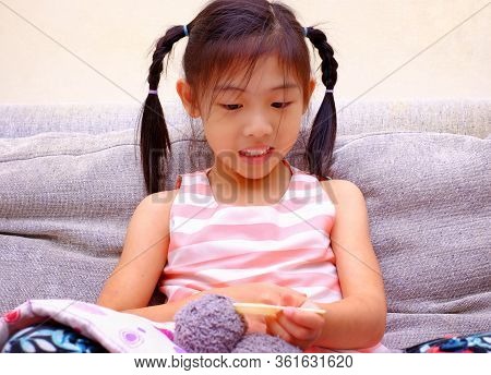 A Cute Asian Girl Playing Nurse With Her Teddy Bear. Feeding Medicine With A Small Spoon.