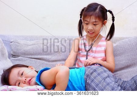 A Young Asian Girl Pretending To Be A Doctor And Taking Care Of Her Sick Sister.