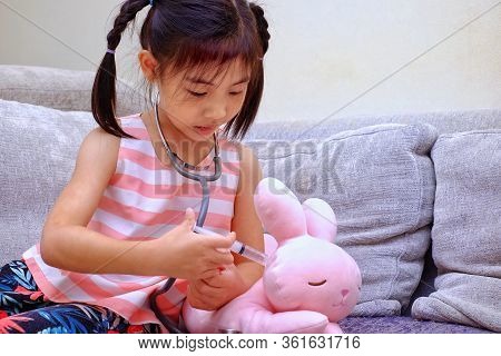 A Young Asian Girl Playing Doctor, Giving Medicine To Her Toy Rabbit Using Syringe