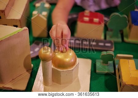 A Child Adding A Wooden Mosque Block To Her Modeled City With Road, Buildings And Trees
